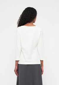 White long-sleeve top with a wide neckline, smooth texture, soft fabric, and a loose fit, paired with a dark gray skirt.