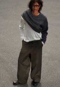 Chemise blanche à manches longues superposée avec un châle en maille gris foncé ; pantalons amples sombres ; chaussures noires ; tenue décontractée texturée.