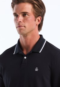 Polo bleu marine en tissu doux avec un col à rayures blanches et bleu clair, doté d'une patte de boutonnage à deux boutons et d'un petit logo de manchot brodé.