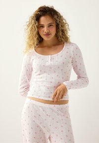 Langærmet, pink, ribbet pyjamastrøje med floral mønster over hele. Rundet halsudskæring og knapdetaljer. Blødt, let bomuldsstof.