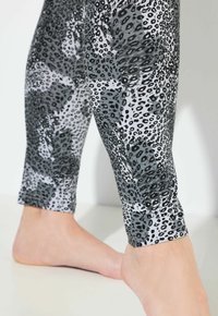 Leggings a stampa animale in nero e grigio, caratterizzati da una texture lucida e una vestibilità aderente, con taglio alla caviglia e una cintura liscia.