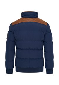 Marineblaue Steppjacke mit einem braunen Lederakzent an der Schulter, hohem Kragen, gerippten Bündchen und gestepptem Paneldesign. Weiche, gepolsterte Textur.