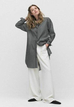 Chemise à rayures noir et blanc, design boutonné, manches longues, associée à un pantalon large blanc et des mocassins noirs.