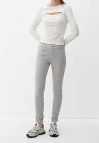 Blusa blanca de manga larga con un corte rectangular; pantalones ajustados gris claro; zapatillas gris y blanca con acentos negros; textura suave.