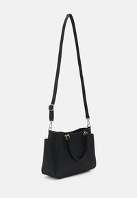 Sac fourre-tout noir en matériau lisse, doté de deux poignées courtes, d'une longue sangle ajustable et d'accents en métal doré.