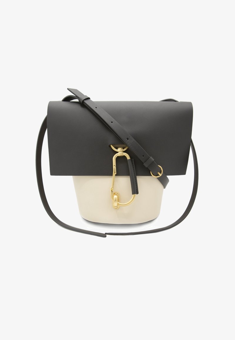 Schwarze und cremefarbene Ledertasche mit Umschlagklappe, verstellbarem Riemen und goldenen Beschlägen, darunter ein Clip und ein Anhänger.