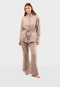 Beżowy zestaw odzieży domowej składający się z rozpinanej bluzy z kapturem z regulowanym ściągaczem w talii oraz rozszerzanych spodni, wykonany z miękkiego, teksturowanego materiału.