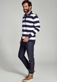 Navy og hvide stribede langærmede polo-shirt, parret med mørke denimjeans og brune snøresko, med oprevne ærmer.