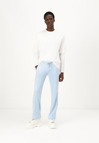 Pantaloni azzurri con cordoncino, dotati di cuciture laterali e una vestibilità rilassata, abbinati a una camicia bianca a maniche lunghe e sneaker bianche chunky.