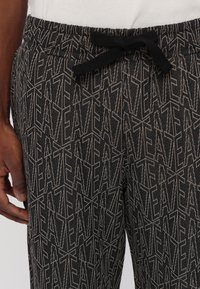 Černé a šedé tepláky se geometrickým vzorem, elastickým pasem se šňůrkou a měkkou, texturovanou tkaninou.