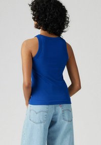 Canotta blu a coste con spalline larghe e un design aderente, abbinata a jeans in denim chiaro con tasche posteriori e dettagli di cucitura.