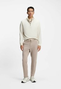 Maglione zip-up color crema chiaro con finitura testurizzata abbinato a pantaloni tapered beige morbidi e sneakers chiare con suole scure.