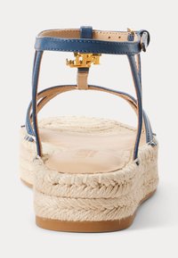 Sandale en cuir bleu avec une semelle en espadrille tissée. Présente un accent en matériel doré près de la bride de cheville et une semelle intérieure lisse et texturée.