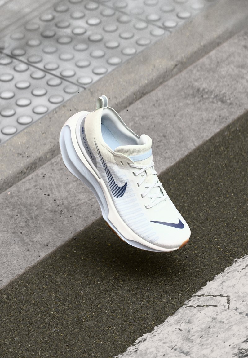 Nike sneakers in white mesh with a textured surface, featuring a navy swoosh logo, rounded sole, and light blue interior.