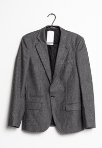 Grå herringbone-blazer på en galge, med en enkel knappstängning, två framfickor och en mjuk svart foder.