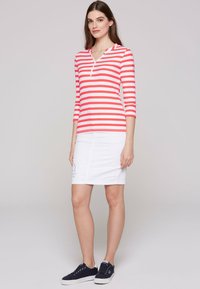Red and white striped long-sleeve top with a collar, paired with a white skirt. Model wears navy sneakers. Textured fabric and fitted shape.