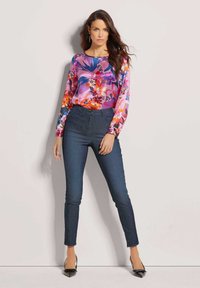 Bloemenmotief langemouwen top in roze en blauwe tinten, gecombineerd met high-waisted donkerdenim jeans. Bevat een getailleerd model en gedessineerde stofdetails.