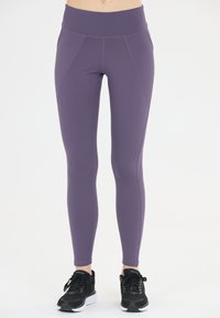 Lila högmidjade leggings tillverkade av elastiskt material, med detaljering på sid sömmarna och en mjuk yta. Parat med svarta sportskor.