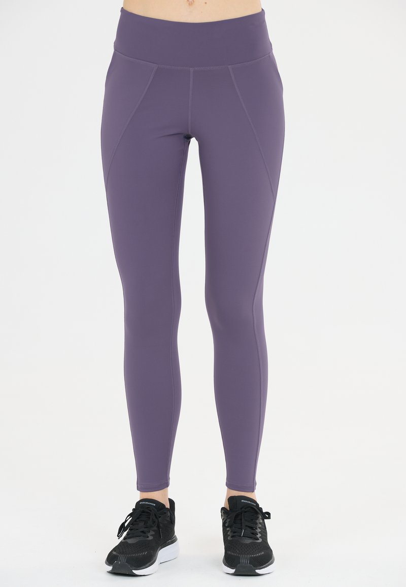 Lila högmidjade leggings tillverkade av elastiskt material, med detaljering på sid sömmarna och en mjuk yta. Parat med svarta sportskor.