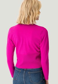 Figurbetontes rosa Sweatshirt mit langen Ärmeln, geripptem Material an Buste und Taille, kombiniert mit hoch geschnittenen Jeans.