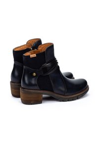 Botines negros de cuero con un panel texturizado, un tacón de madera marrón y una correa decorativa negra alrededor del tobillo.