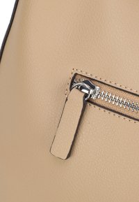 Beige Lederhandtasche mit strukturierter Oberfläche, ausgestattet mit einem oberen Reißverschluss aus silbernem Metall und einem beigen Reißverschlussanhänger.
