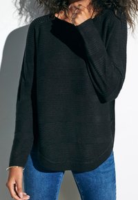 Maglione nero realizzato in un tessuto a maglia texturizzato, con una vestibilità comoda, scollatura larga e maniche lunghe, abbinato a jeans in denim blu.