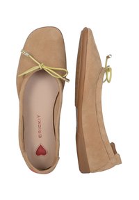 Ballerines en suède beige avec un bout carré, un accent en nœud jaune avec un matériel doré, et un détail en forme de cœur rouge sur la semelle intérieure.