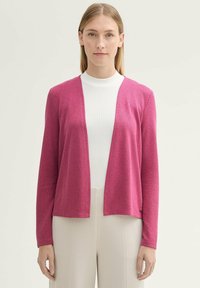 Fuchsia cardigan i texturerad stickad kvalitet, öppen frontdesign, långa ärmar och en knappdetalj på fållen, kombinerad med en vit topp och beige byxor.