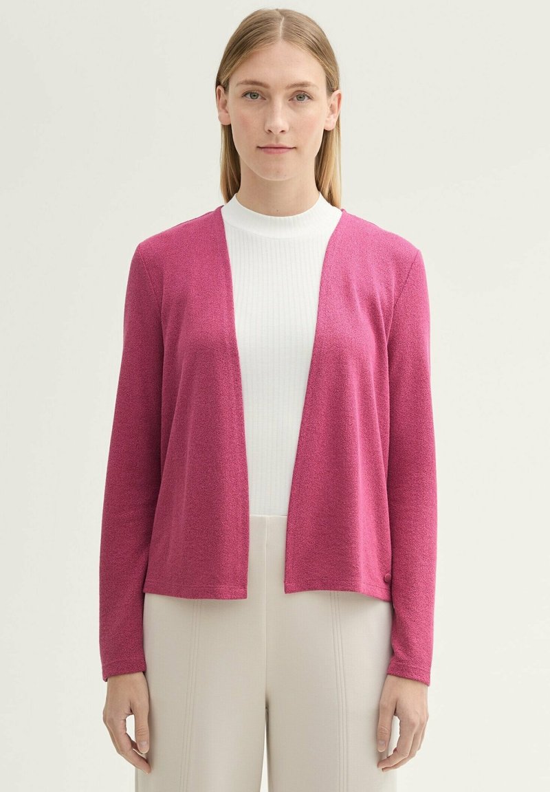 Fuchsia cardigan i texturerad stickad kvalitet, öppen frontdesign, långa ärmar och en knappdetalj på fållen, kombinerad med en vit topp och beige byxor.