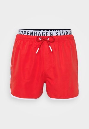 Pantaloni de baie roșii cu margine albă, talie elastică cu text "COPENHAGEN STUDIOS", șnur ajustabil cu capete albe.