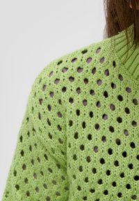 Maglione lavorato a maglia di un brillante verde, caratterizzato da un design a rete con motivi esagonali e un collo alto. La texture è morbida e leggera.
