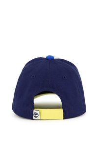 Cappello blu navy con una fascia gialla e apertura posteriore. Presenta un bottone blu sulla parte superiore e un'etichetta con logo di lato. Realizzato in tessuto morbido.