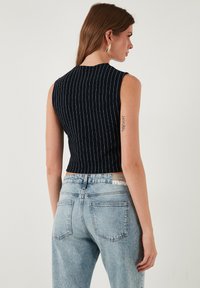 Top bez rukávov v námorníckej modrej farbe s vertikálnymi bielymi pruhmi, priliehavý strih a skrátená dĺžka, skombinovaný so svetlomodrými džínsy s vysokým pásom.