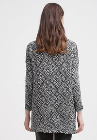 Czarnobiały top z długim rękawem o luźnym kroju, z geometrycznym wzorem i okrągłym dekoltem. Wykonany z teksturowanej tkaniny.