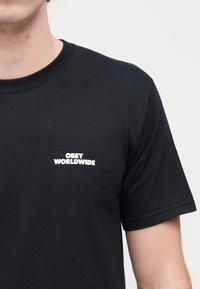 Μαύρο βαμβακερό μπλουζάκι με κοντά μανίκια, με λευκό κείμενο "OBEY WORLDWIDE" στο αριστερό μέρος του στήθους. Απλή, στρογγυλή λαιμόκοψη.