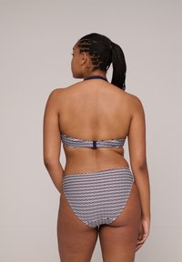 Dwuczęściowy kostium kąpielowy w granatowo-białym wzorze fal. Góra ma projekt na szyję, a dół ma wysoki stan.