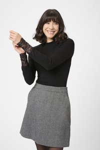 Black ribbed long-sleeve top with lace accents on cuffs, paired with a gray houndstooth-patterned skirt. Neutral backdrop.