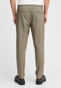 Brune teksturerte bukser med rett ben-design, elastisk liv, og to baklommer. Brukt med mørke sko.