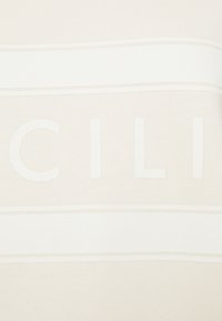 Beige stickad tyg har djärva vita bokstäver i centrum med horisontella vita ränder ovanför och nedanför, vilket skapar en ren design.