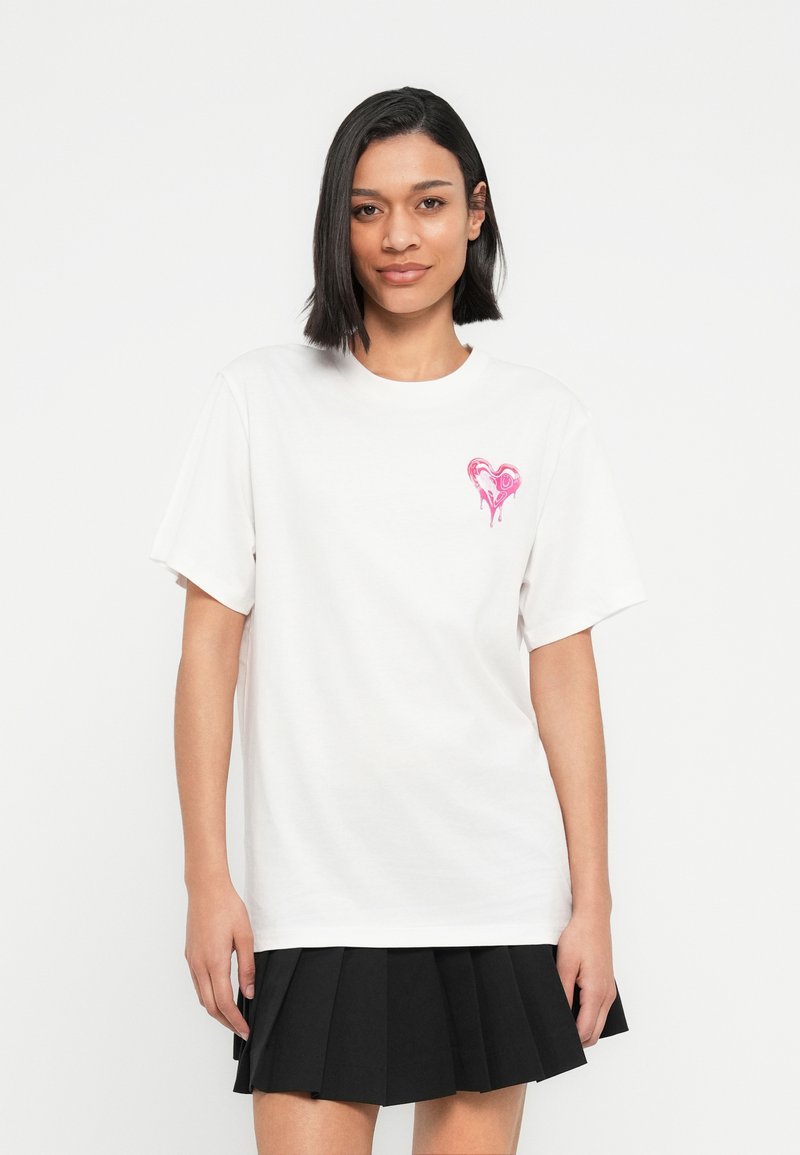 Λευκό βαμβακερό t-shirt με ροζ καρδιά στο αριστερό στήθος. Κοντά μανίκια και στρογγυλή λαιμόκοψη. Απλή, άνετη γραμμή.