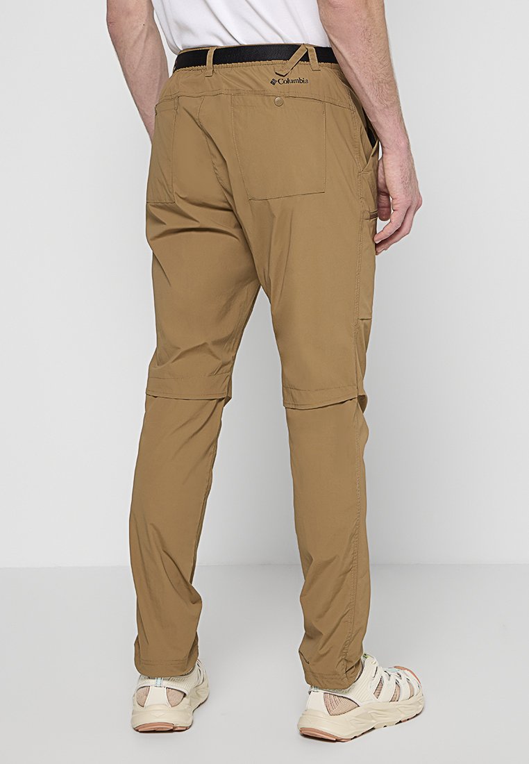 Homme portant un pantalon de randonnée convertible tan de Columbia et des baskets beiges, se tenant devant un fond blanc uni.