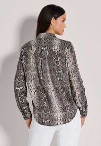 Langärmlige Bluse im Schlangenprint-Muster in den Farben Beige, Braun und Schwarz, mit Knopfverschluss hinten und weichem Stoffgefühl.