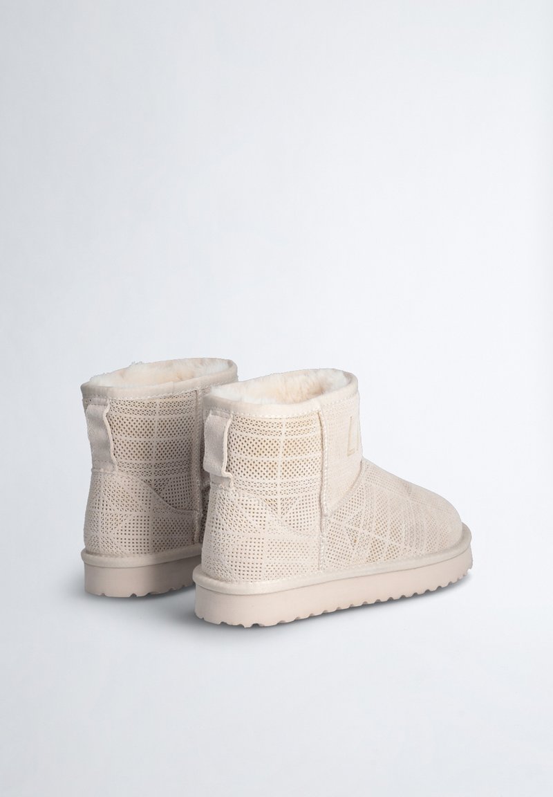 Beige Knöchelstiefel mit einer perforierten Textur, weicher Innenausstattung und flexibler Außensohle, mit einem Logo-Detail an der Seite.