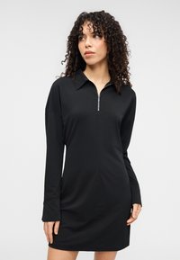 Μαύρο φόρεμα με φερμουάρ μπροστά από απαλό ύφασμα, με μυτερό γιακά, μακριά μανίκια και μινιμαλιστικό σχέδιο με ένα μόνο διακριτικό κουμπί.