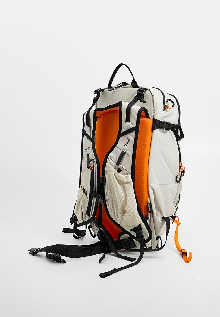 Mochila con un exterior beige, interior naranja, múltiples correas ajustables y bolsillos de malla. Diseñada con varios puntos de sujeción.
