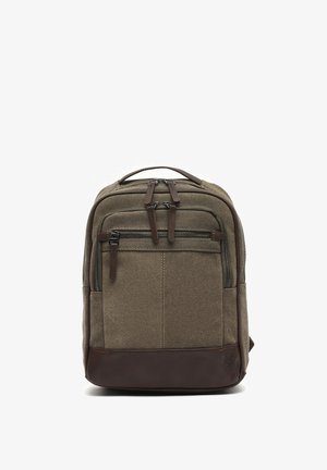 Bruine rugzak van canvas en leer met meerdere ritsvakken en een bovenste draaghandvat, rechtopstaand op een witte achtergrond.