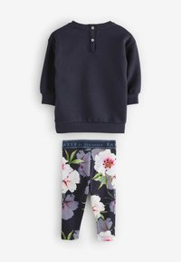 Marinefarbener Sweatshirt mit rundem Halsausschnitt und zwei Knöpfen hinten, kombiniert mit Leggings im Blumenmuster mit großen weißen und rosa Blumen.