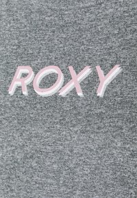 Heather šedé tričko s nápisem "ROXY" vytištěným v růžové a bílé. Textilie je měkká a mírně strukturovaná, ideální pro každodenní nošení.