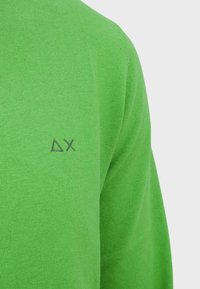 Maglione verde lavorato a maglia con scollatura rotonda e un piccolo logo grigio sul lato sinistro. Texture morbida e vestibilità casual.